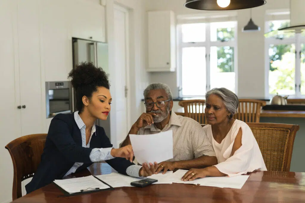 A couple and agent talking about paper documents on the brown table and chairs