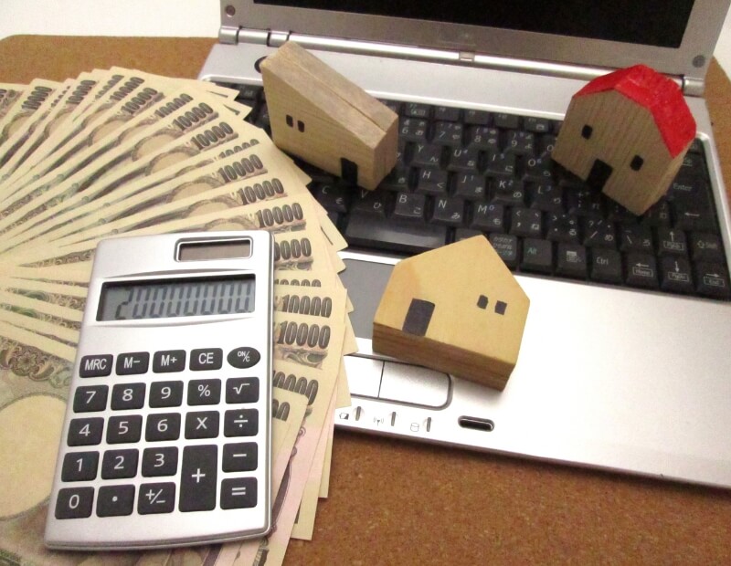 Paper bills, laptop, calculator, and miniature house on top of a table - Home Buy Cash